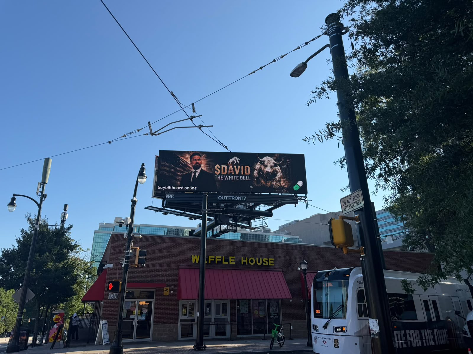 A real digital billboard in Atlanta reading '$DAVID THE WHITE BULL' above a Waffle House restaurant, next to a light rail line