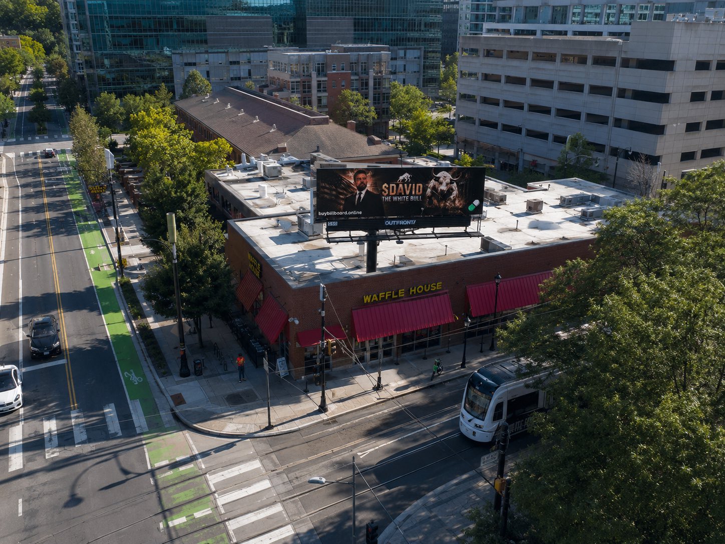 Aerial drone photo of the real $DAVID 'The White Bull' digital billboard mounted above a Waffle House restaurant in Atlanta, next to a light rail line